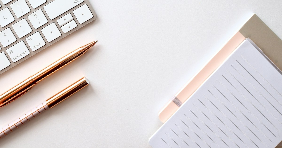 Notebook and pens beside a keyboard on a desk